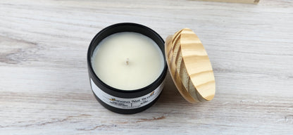 Candle in a black container with a wooden lid on a light wooden surface
