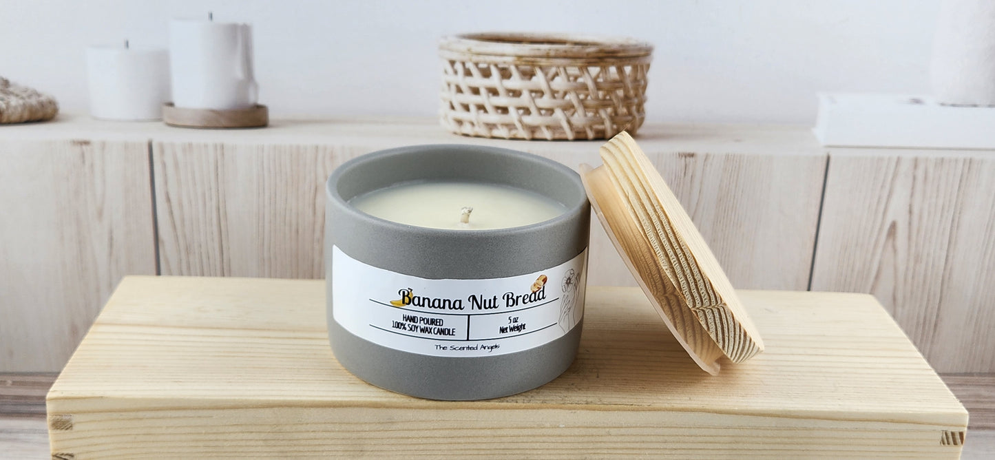 Candle in a gray container with a label on a wooden surface, with a blurred background of a shelf.