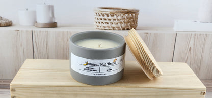 Candle in a gray container with a label on a wooden surface, with a blurred background of a shelf.