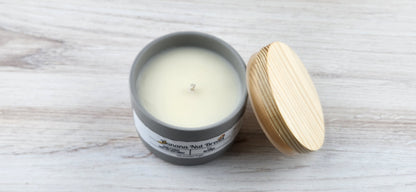 Candle in a gray container with a wooden lid on a light wooden surface