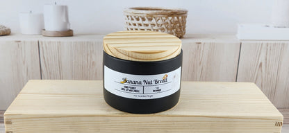 Black candle with wooden lid on a wooden surface, labeled 'Banana Nut Bread'.