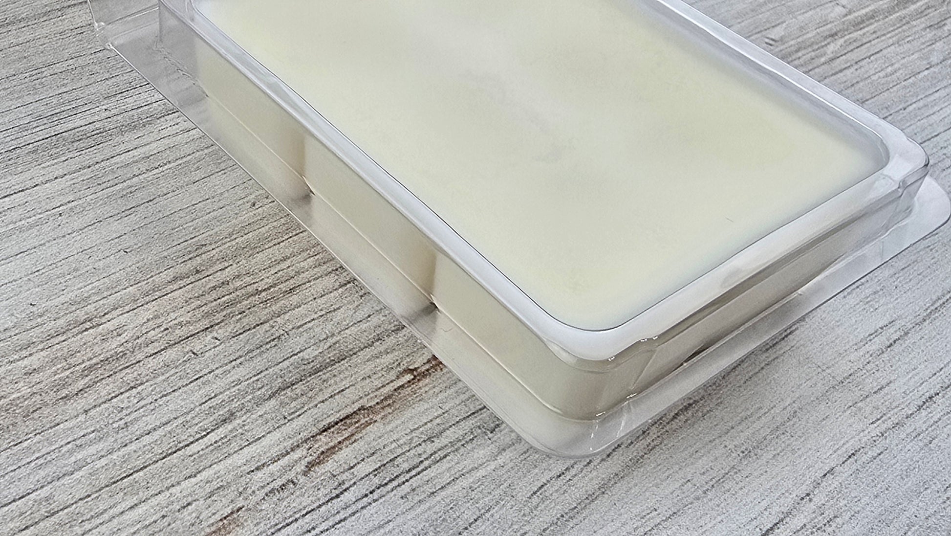 Transparent wax melt container with a white lid on a wooden surface