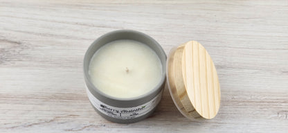 Candle in a gray container with a wooden lid on a light wooden surface