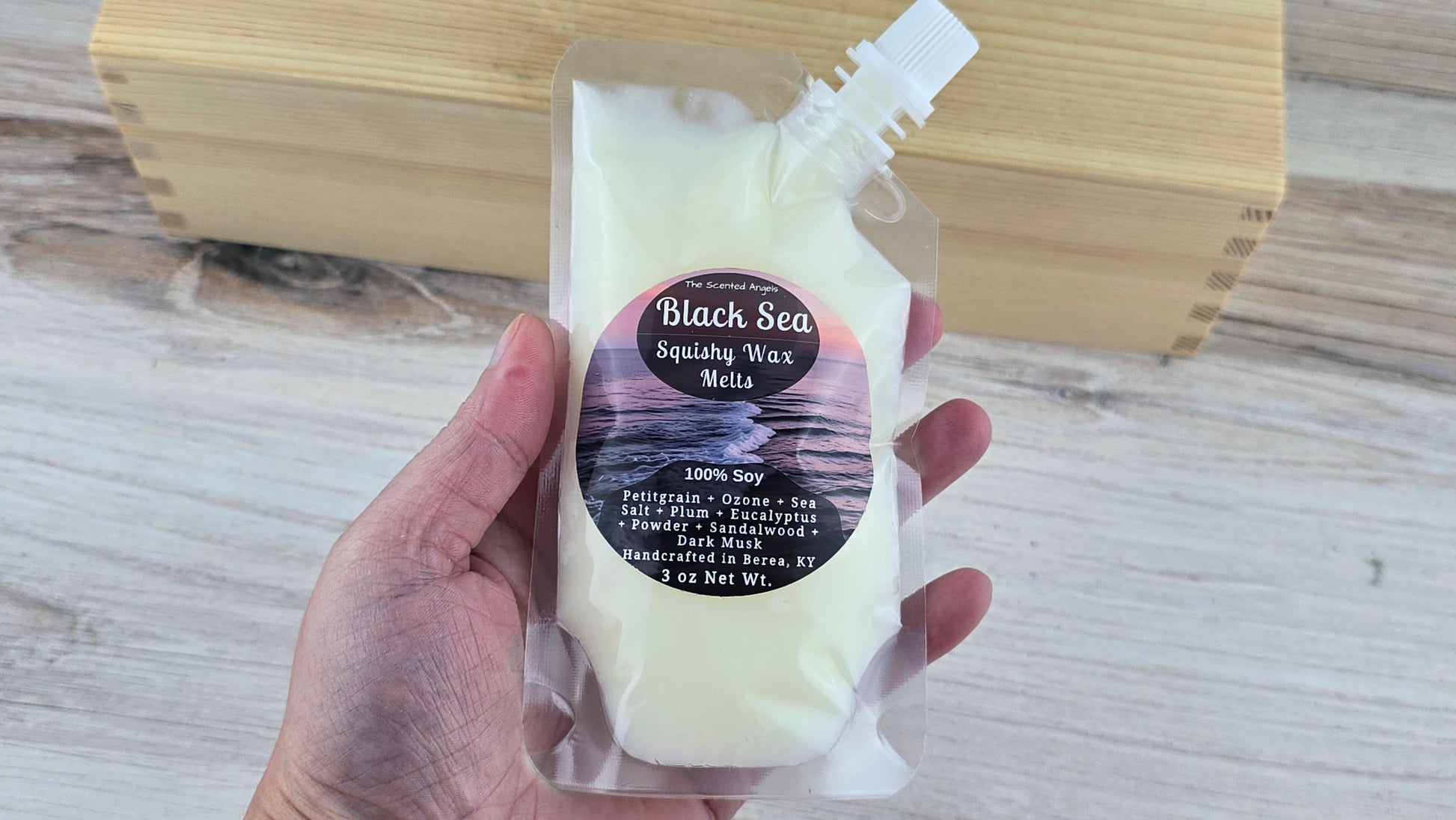 Hand holding a package of Black Sea Squishy Wax Melts on a wooden surface
