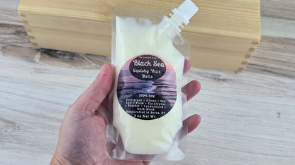 Hand holding a package of Black Sea Squishy Wax Melts on a wooden surface