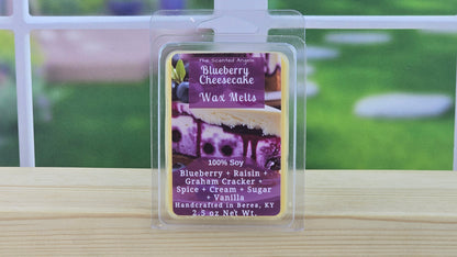 Blueberry Cheesecake wax melt packaging on a wooden surface with a blurred outdoor background