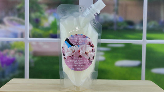 A pouch of 100% soy squeezy wax melts with a 'Cherry Blossom' label, placed on a wooden surface with a garden visible in the background.