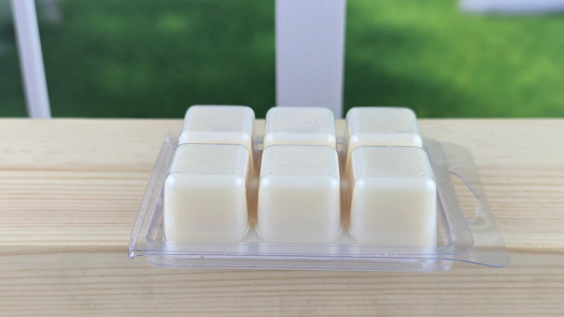Packaged cream-colored wax melts on a wooden surface with a blurred green outdoor background