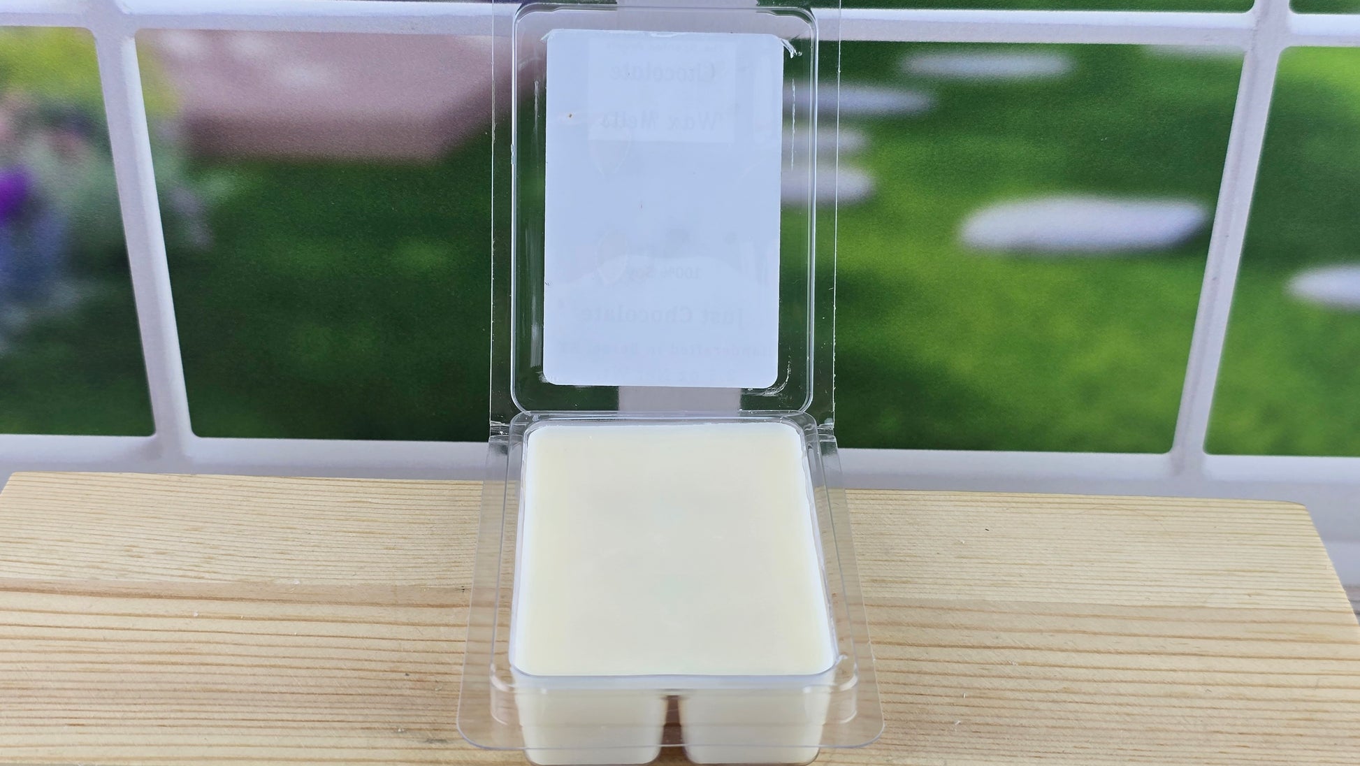 Packaged wax melt clamshell on a wooden surface with a blurred outdoor background