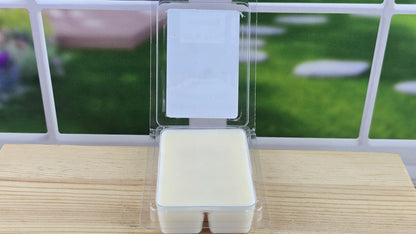 Packaged wax melt clamshell on a wooden surface with a blurred outdoor background
