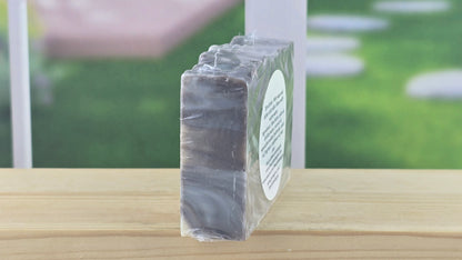 Bar of soap in a clear plastic wrap on a wooden surface with a blurred outdoor background