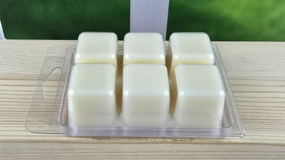 Wax melts in a clear plastic holder on a wooden surface with a blurred green background.