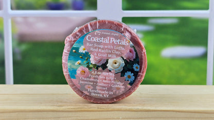 Coastal Petals bar soap with Luffa, Red Kaolin Clay, and Goat Milk on a wooden surface with a blurred outdoor background.