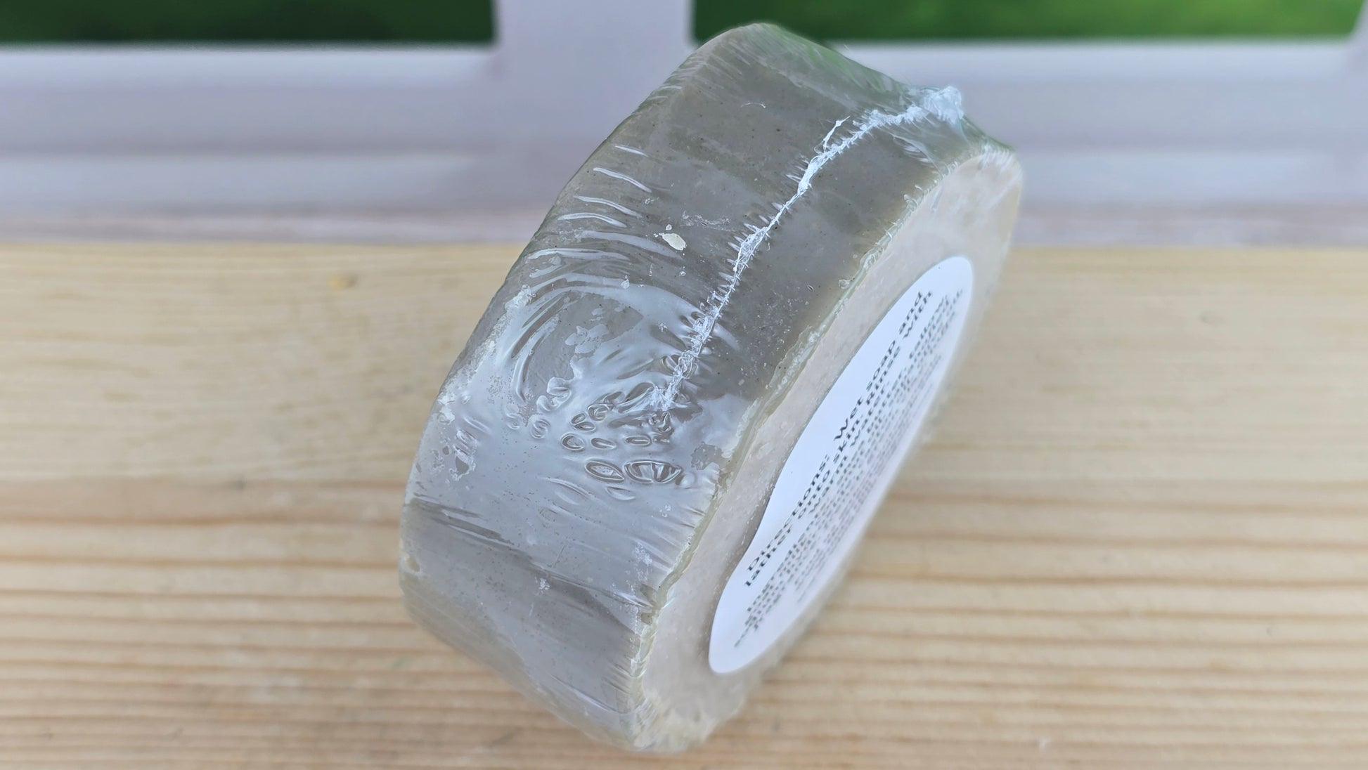 Roll of Coastal Serenity bar soap with Luffa, French Green Clay and Goat Milk on a wooden surface with a blurred background