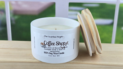 A white soy wax candle with a label reading 'Coffee Shop', accompanied by a hand-cut pine wood lid, set on a wooden surface with a bright background.