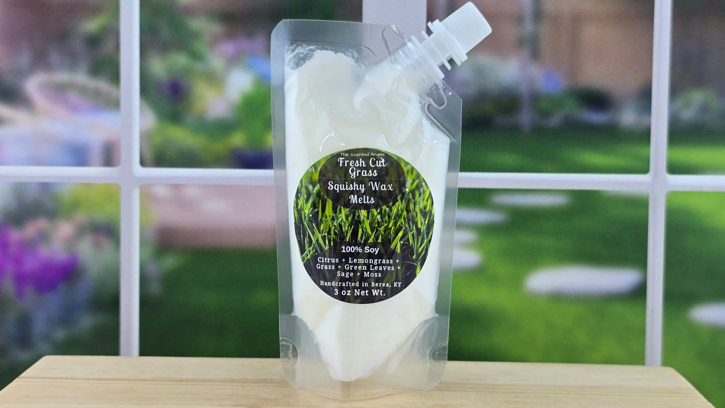 Packaged Fresh Cut Grass Squishy Wax Melts with grass on a wooden surface, blurred outdoor background
