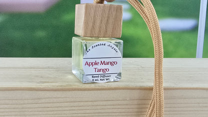 Perfume bottle labeled 'Apple Mango Tango' on a wooden surface with a blurred background.