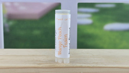 Lip balm tube labeled 'Mango Peach Fusion' on a wooden surface with a blurred outdoor background.