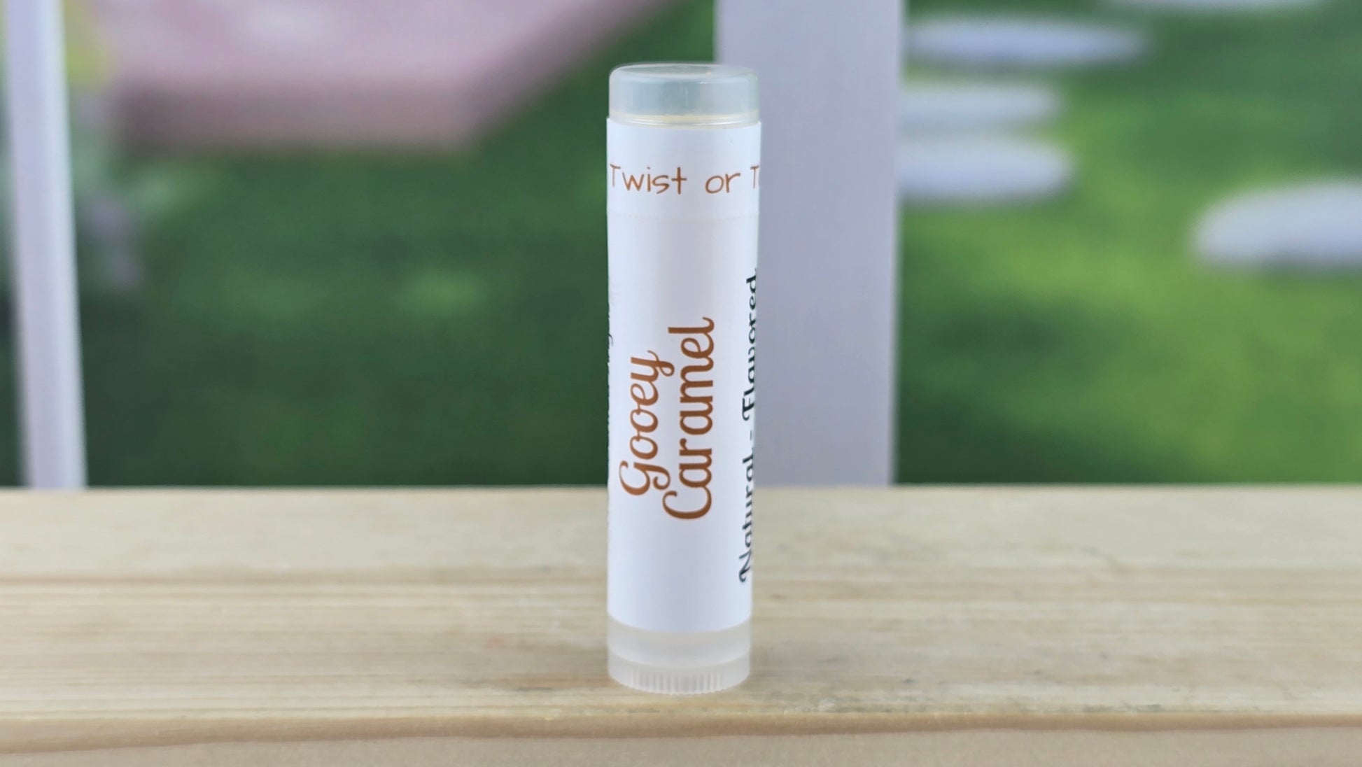 Lip balm tube labeled 'Creeey Caramel' on a wooden surface with a blurred outdoor background