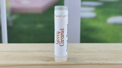 Lip balm tube labeled 'Creeey Caramel' on a wooden surface with a blurred outdoor background