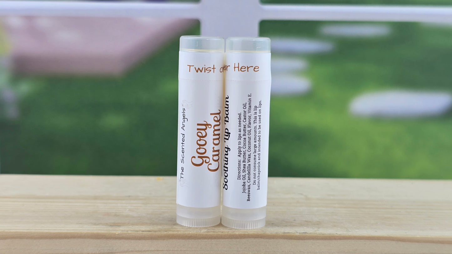 Two lip balm tubes labeled 'Goopy Caramel' and 'Twist or Here' on a wooden surface with a blurred outdoor background.