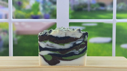 A bar of handmade soap set on a wooden surface with a bright window in the background.
