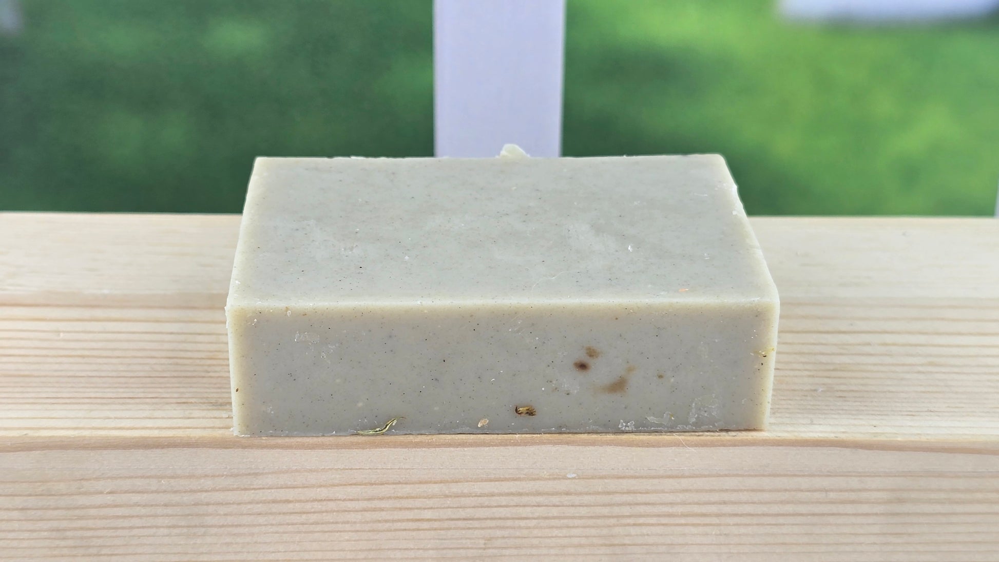 Bar of soap on a wooden surface with a blurred green outdoor background