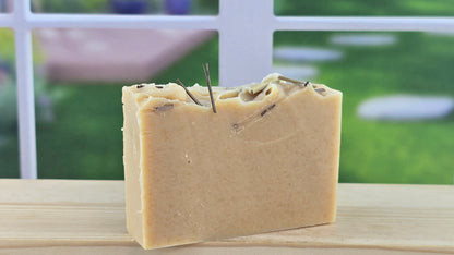 Lemongrass Essential Oil Bar of soap with visible herbs on a wooden surface with a blurred outdoor background