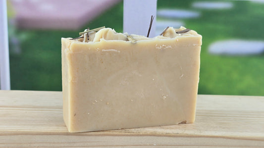Lemongrass Essential Oil Bar of soap with greenery on top, placed on a wooden surface with a blurred outdoor background