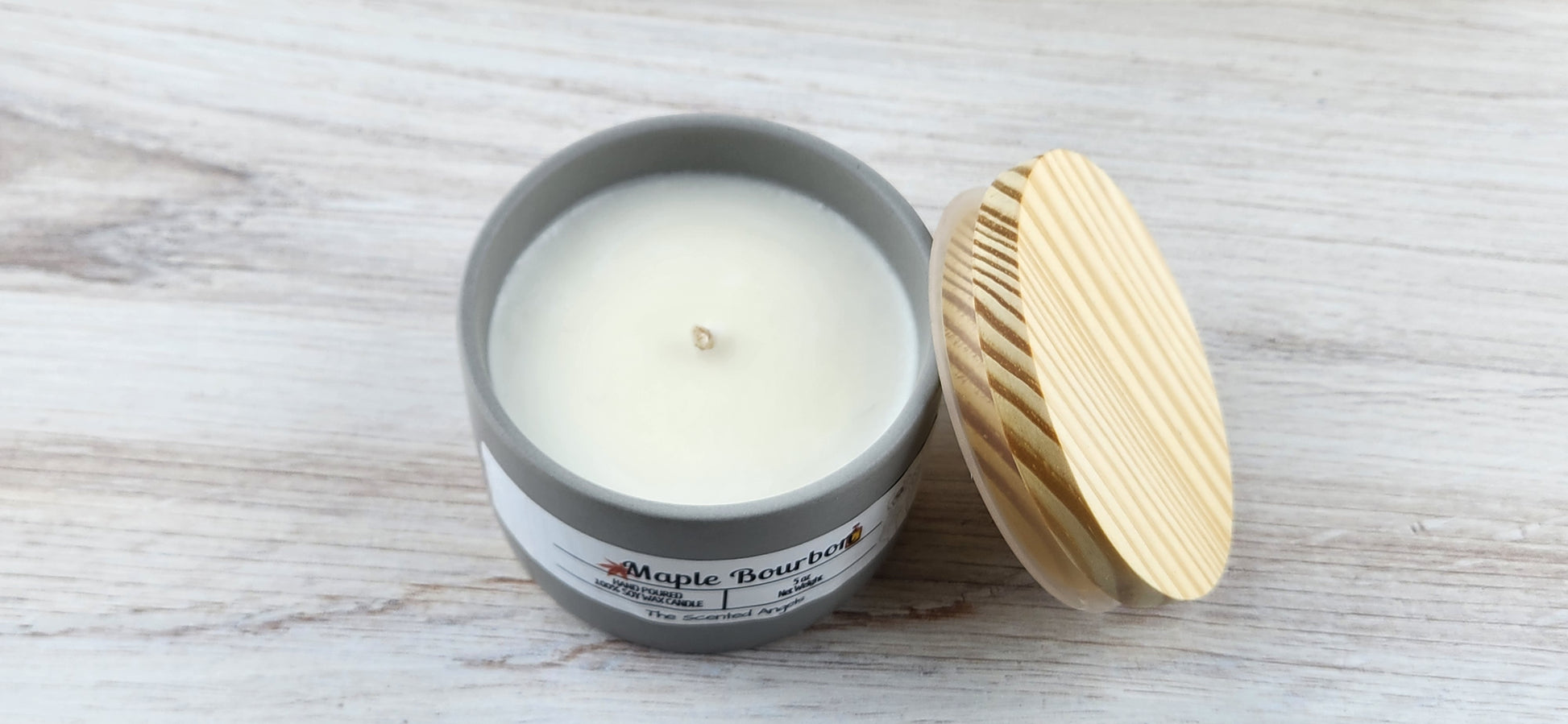 Candle in a gray container with a wooden lid on a light wooden surface