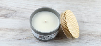 Candle in a gray container with a wooden lid on a light wooden surface