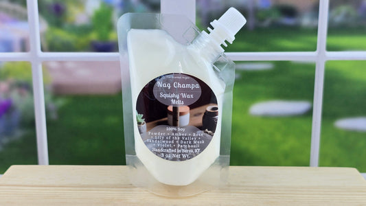 A clear plastic pouch containing white squeezable wax melts with a label that reads 'Nag Champa', with a blurred background.