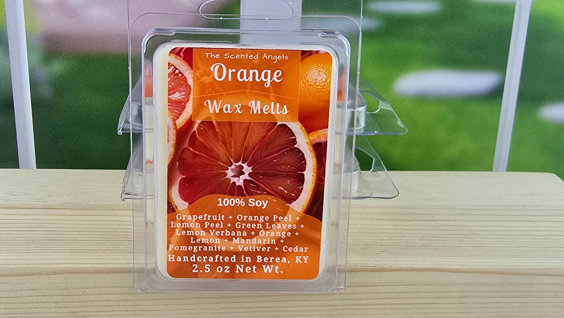 Orange wax melt packaging on a wooden surface with grass in the background
