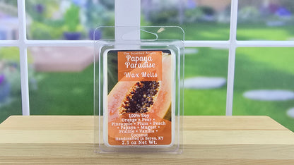 Papaya Paradise wax melt packaging on a wooden surface with a blurred outdoor background