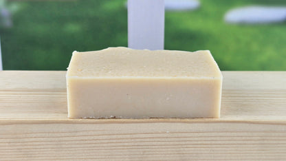 bottom view of Plain Jane Bar of soap on a wooden surface with a blurred green outdoor background
