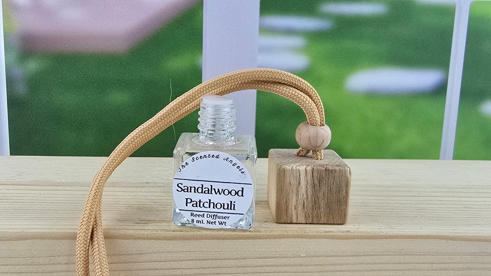 Bottle of sandalwood patchouli diffuser oil with a wooden diffuser on a windowsill.