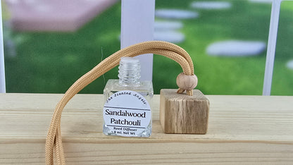 Bottle of sandalwood patchouli diffuser oil with a wooden diffuser on a windowsill.