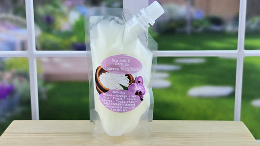 A clear plastic pouch filled with white wax melts, labeled 'Sea Salt & Orchids', placed on a wooden surface with a green, floral background.