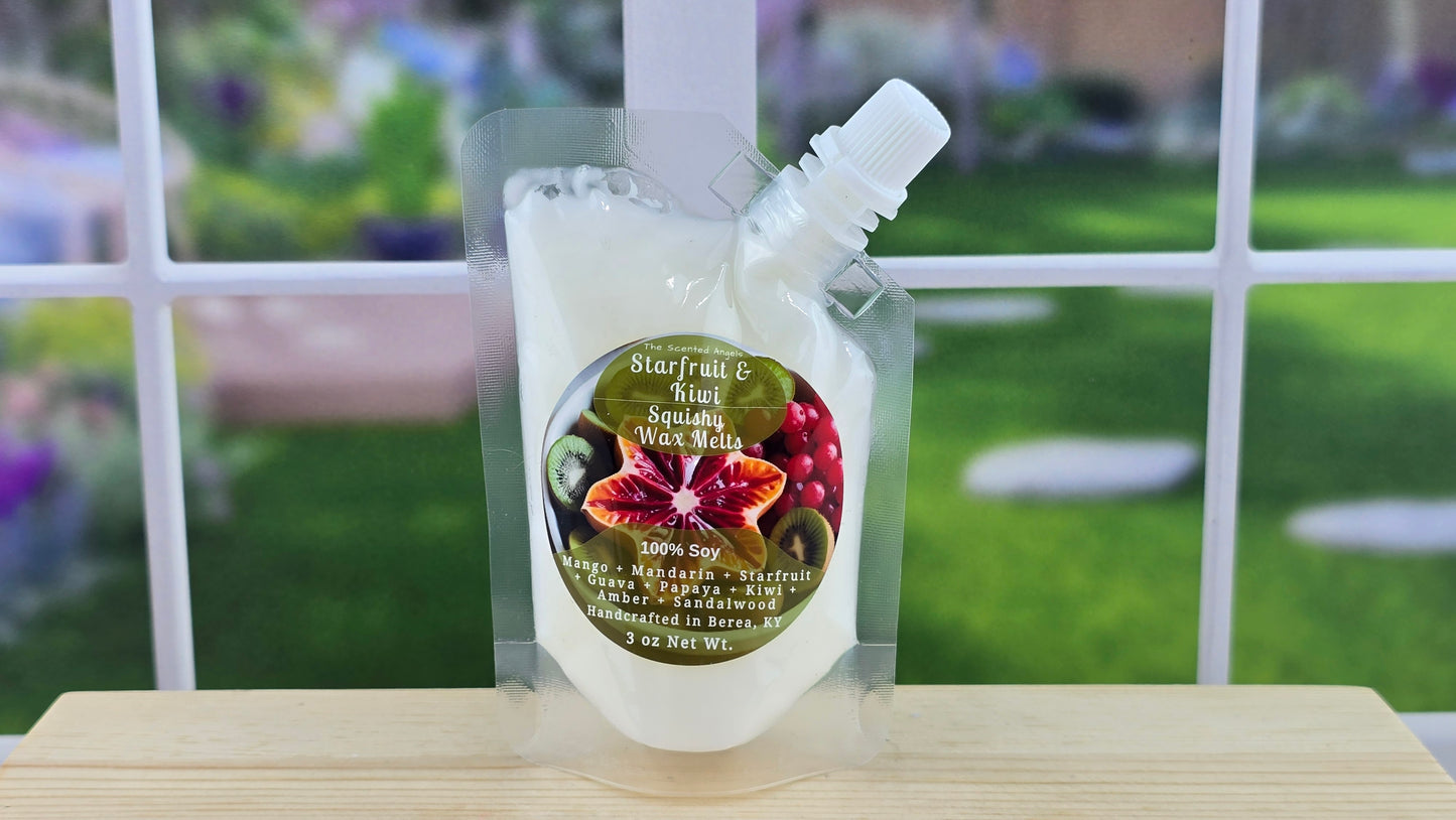 A clear plastic pouch containing white wax melts with a squeezable dispenser top, labeled 'Starfruit & Kiwi 100% Soy', placed on a wooden surface with a blurred greenery background.