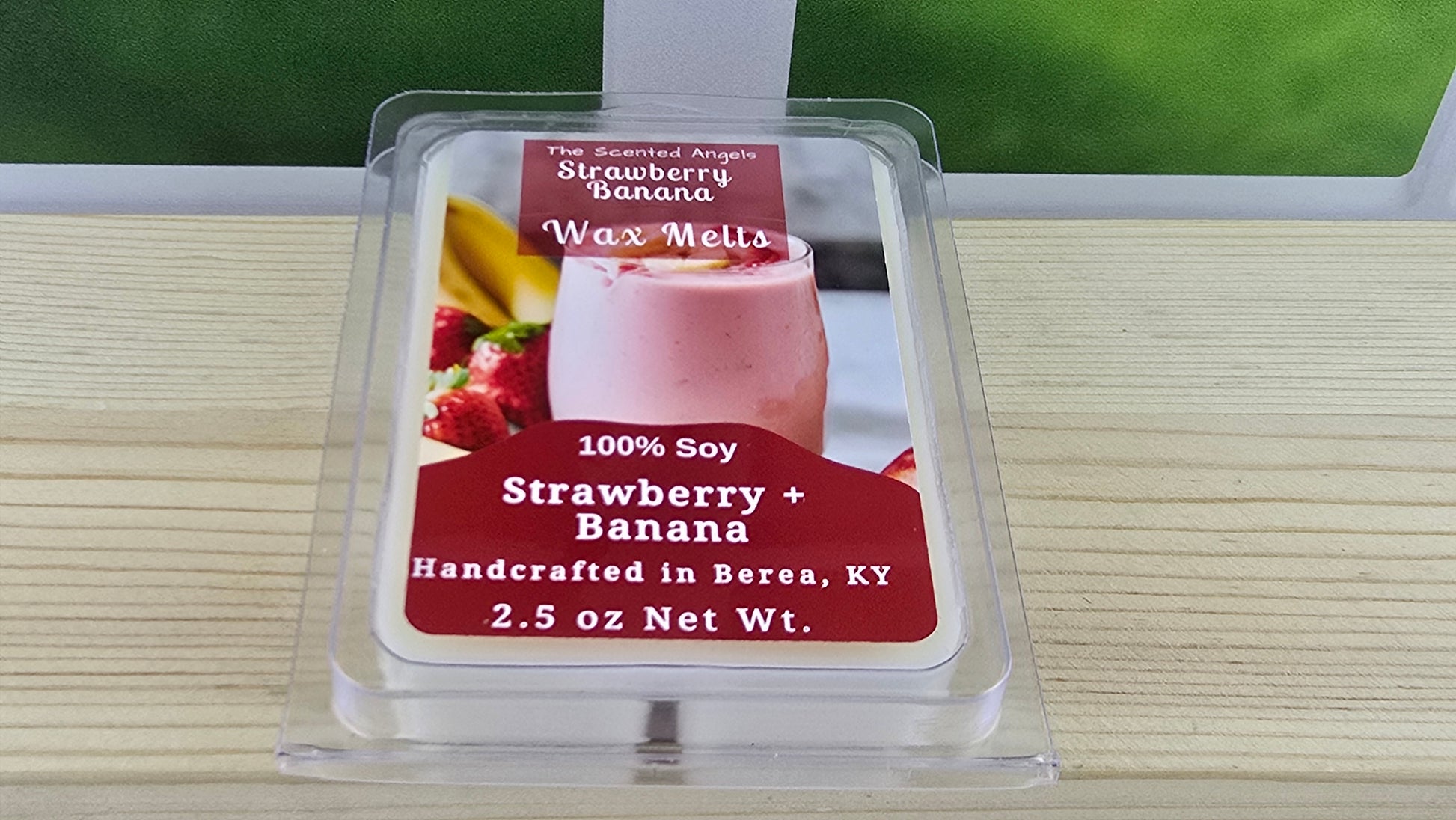 Strawberry Banana wax melt packaging on a wooden surface with a blurred green background