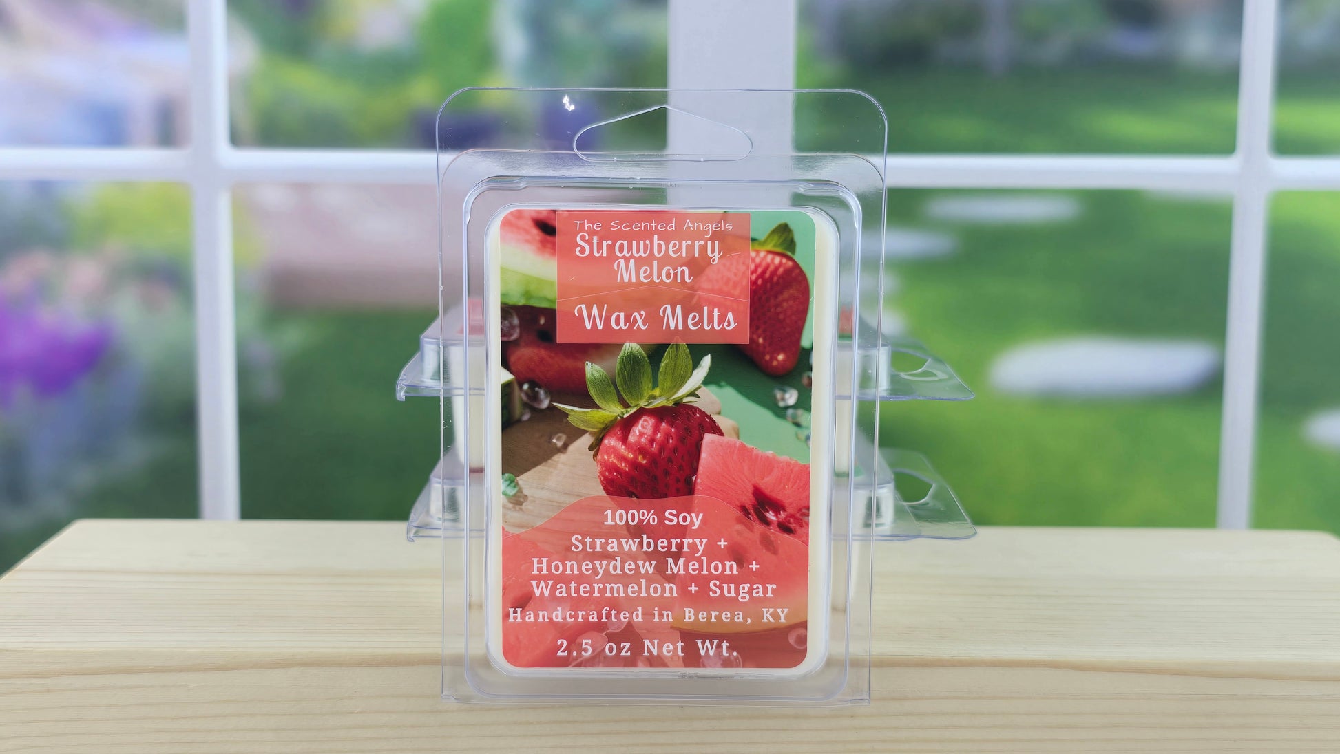 Strawberry Melon wax melt packaging on a wooden surface with a blurred outdoor background