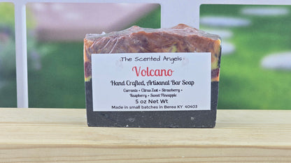 Handcrafted soap bar labeled 'Volcano' by 'The Scented Angels' on a wooden surface with a blurred outdoor background.