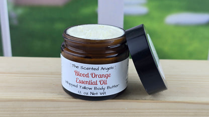 A jar of blood orange essential oil with a black lid, labeled with a white and green label, on a wooden surface with a bright background.