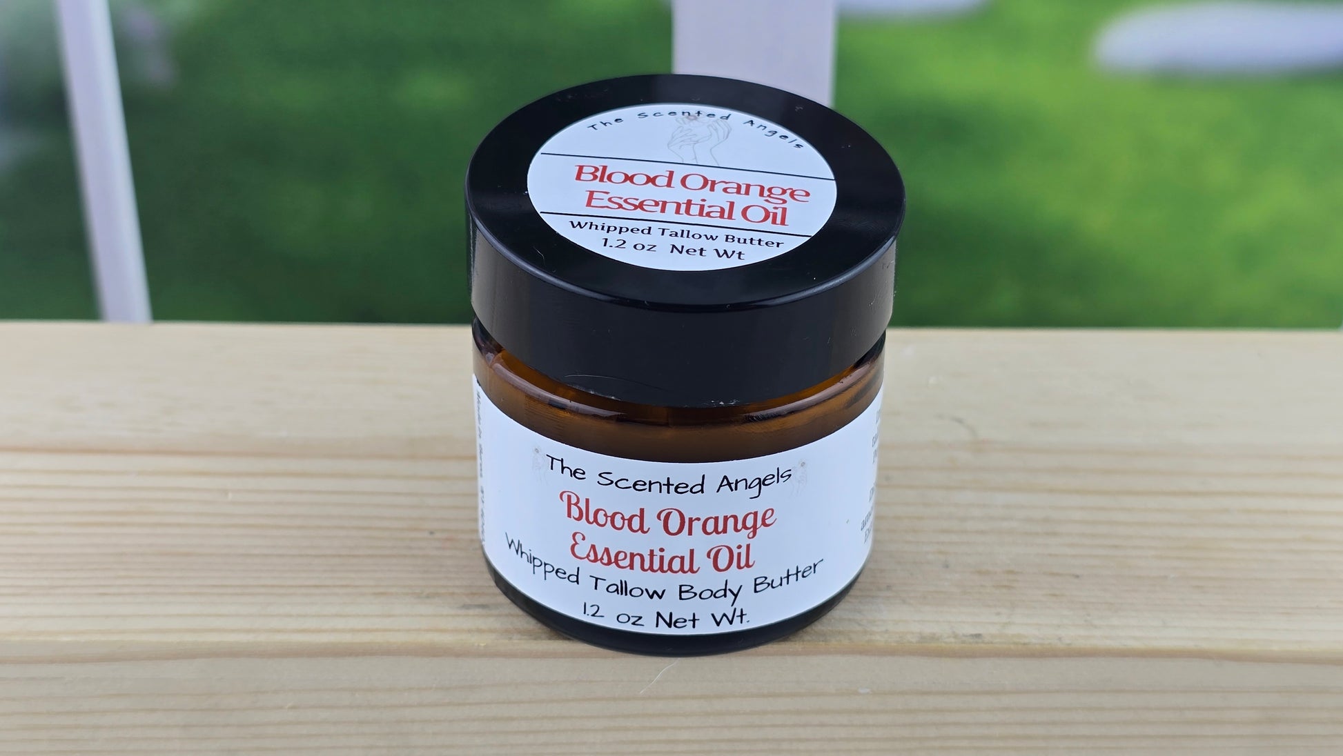Jar of blood orange essential oil whipped tallow body butter on a wooden surface.