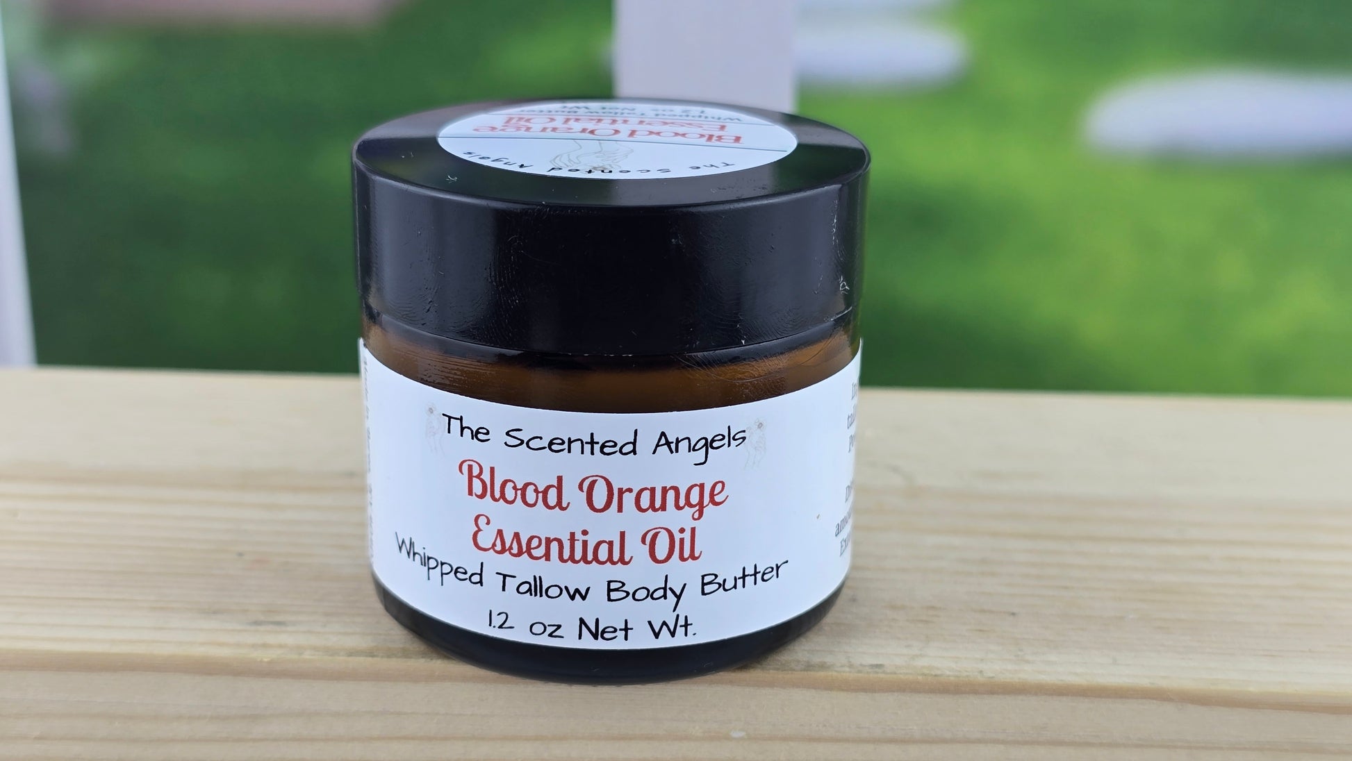 Jar of blood orange essential oil whipped tallow body butter on a wooden surface.