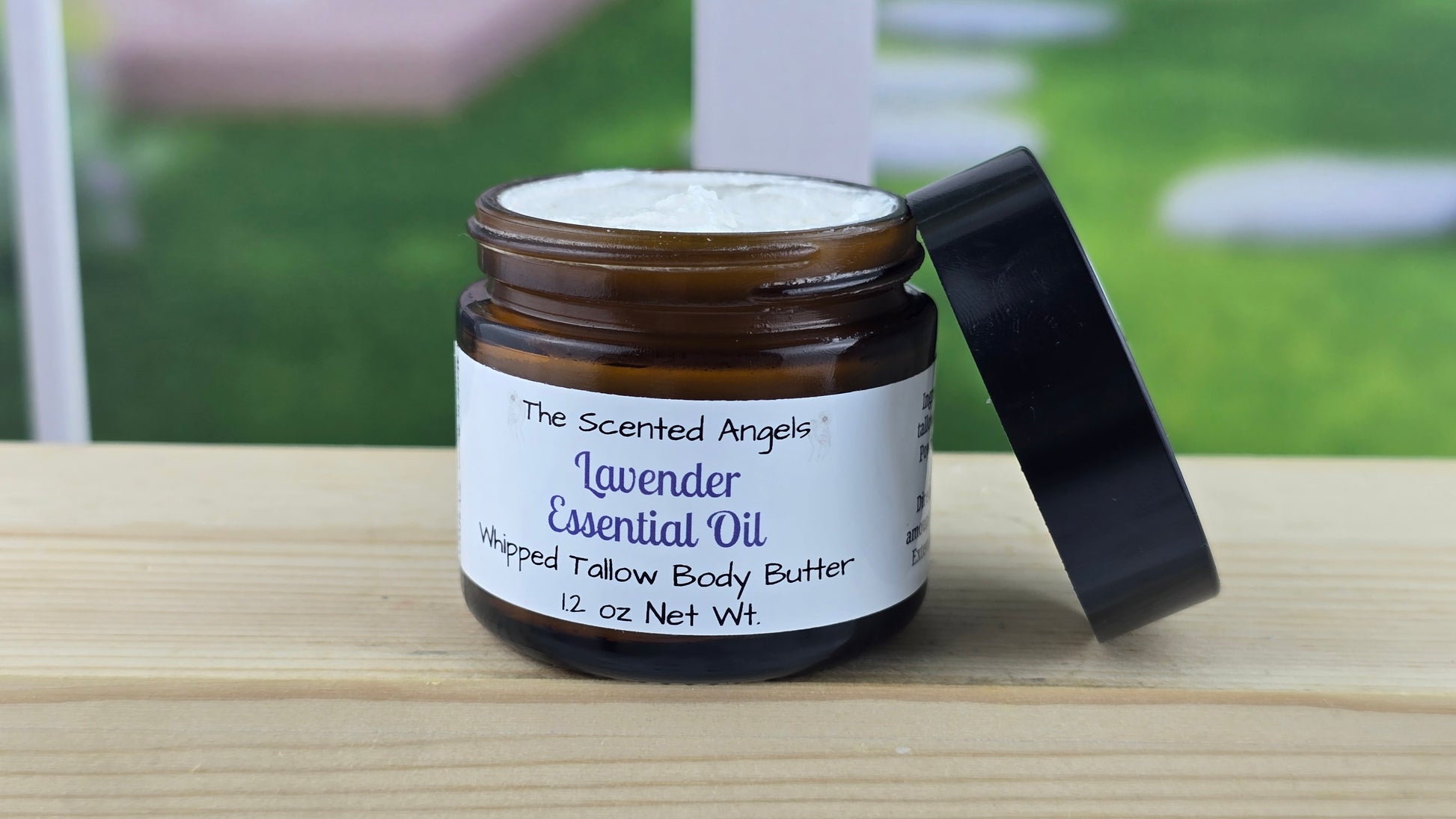 A jar of Lavender essential oil with a black lid, labeled with a white and green label, on a wooden surface with a bright background.