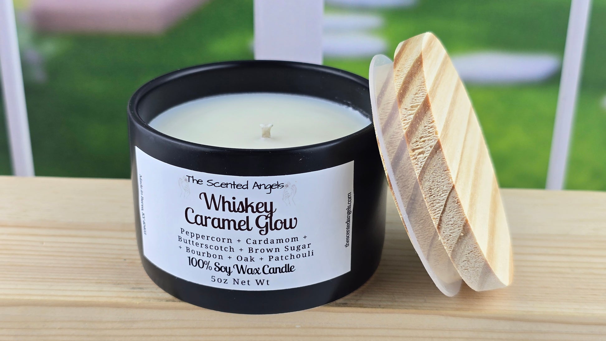 A 5 oz soy wax candle with a label that reads 'Whiskey Caramel Glow', featuring a black matte vessel and a hand-cut pine wood lid, set on a wooden surface.
