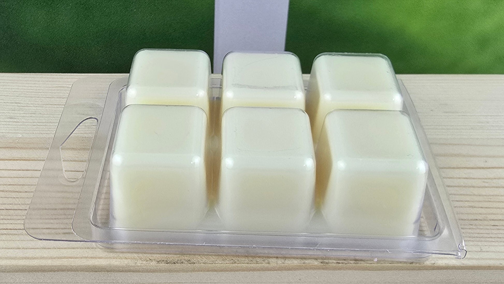 Four wax melts in a clear plastic container on a wooden surface with a green blurred background