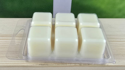 Four wax melts in a clear plastic container on a wooden surface with a green blurred background