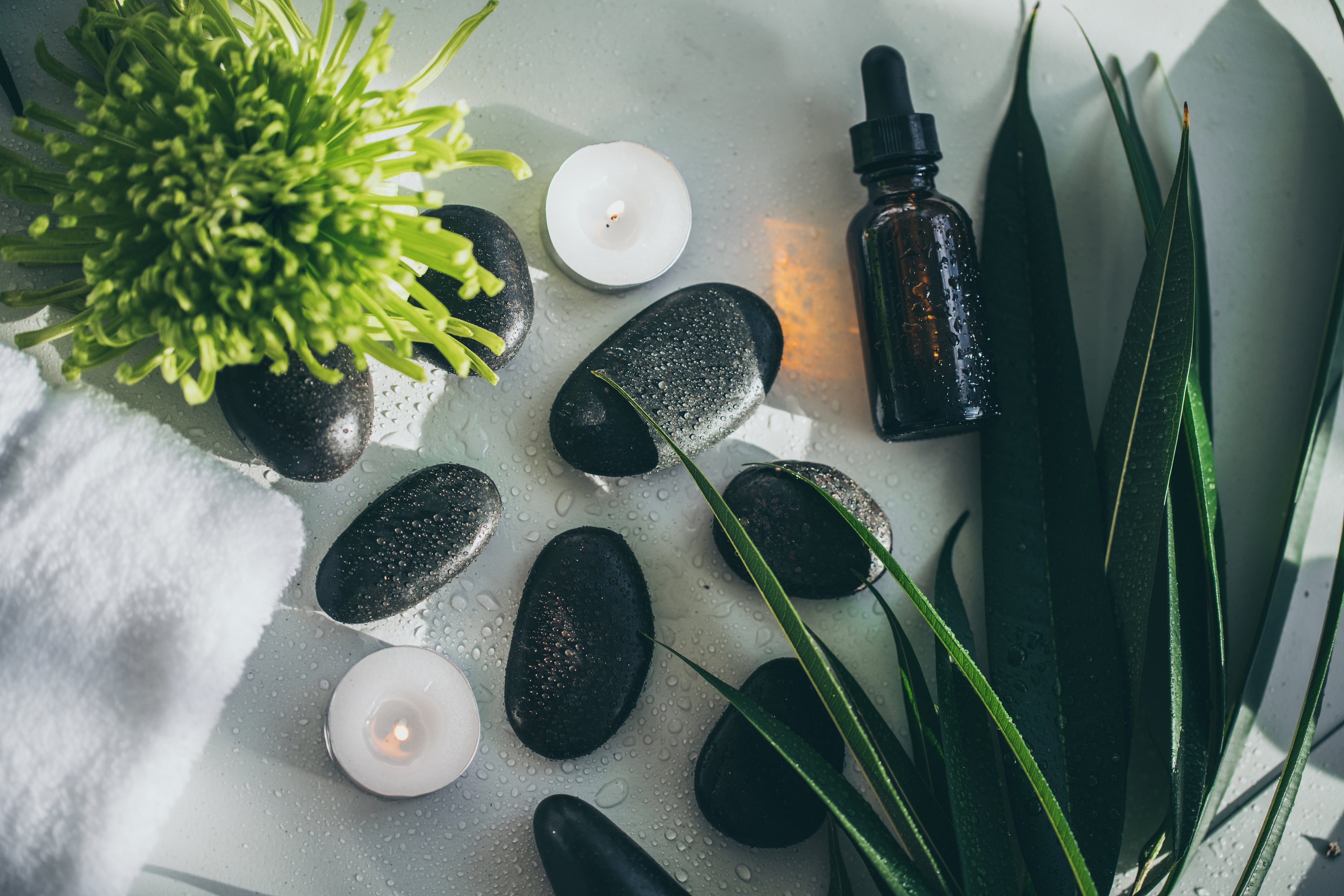 Aromatherapy setup with essential oil dropper, candles, and stones on a light surface.